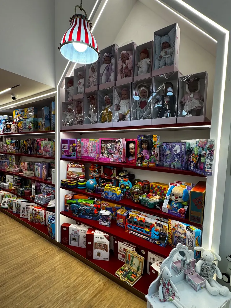 Boxed dolls on the top shelves and toys on the shelves below, inside the white house-shaped frame, with a small white doll's dressing table in front.
